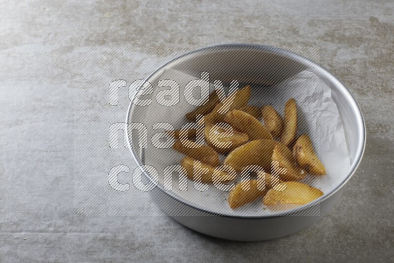 wedges potato on parchment paper in a stainless steel round tray on grey textured counter top