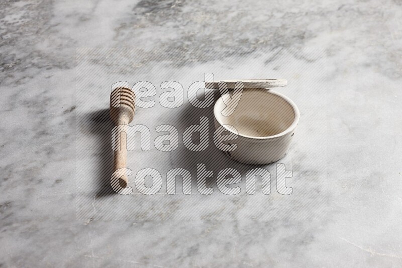 White pottery bowl with wooden honey dipper on the side on grey marble background