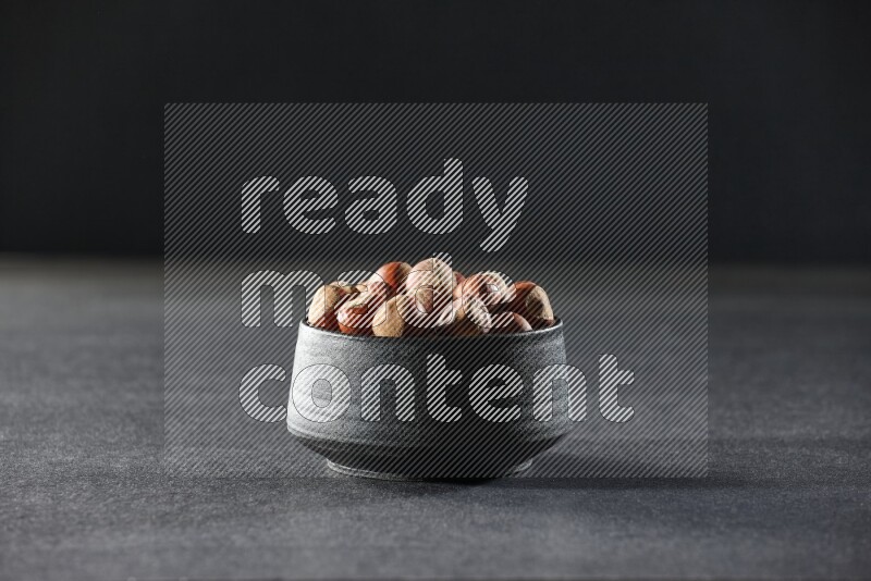 A black pottery bowl full of hazelnuts on a black background in different angles