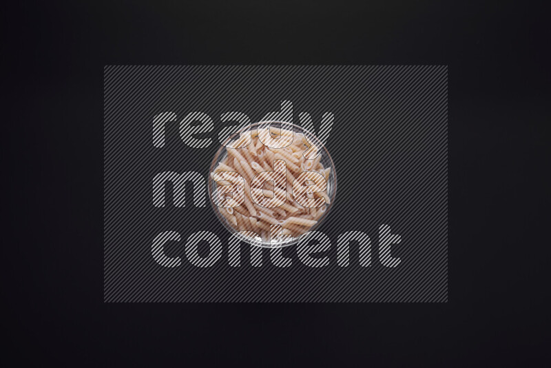 Mini penne pasta in a glass bowl on black background