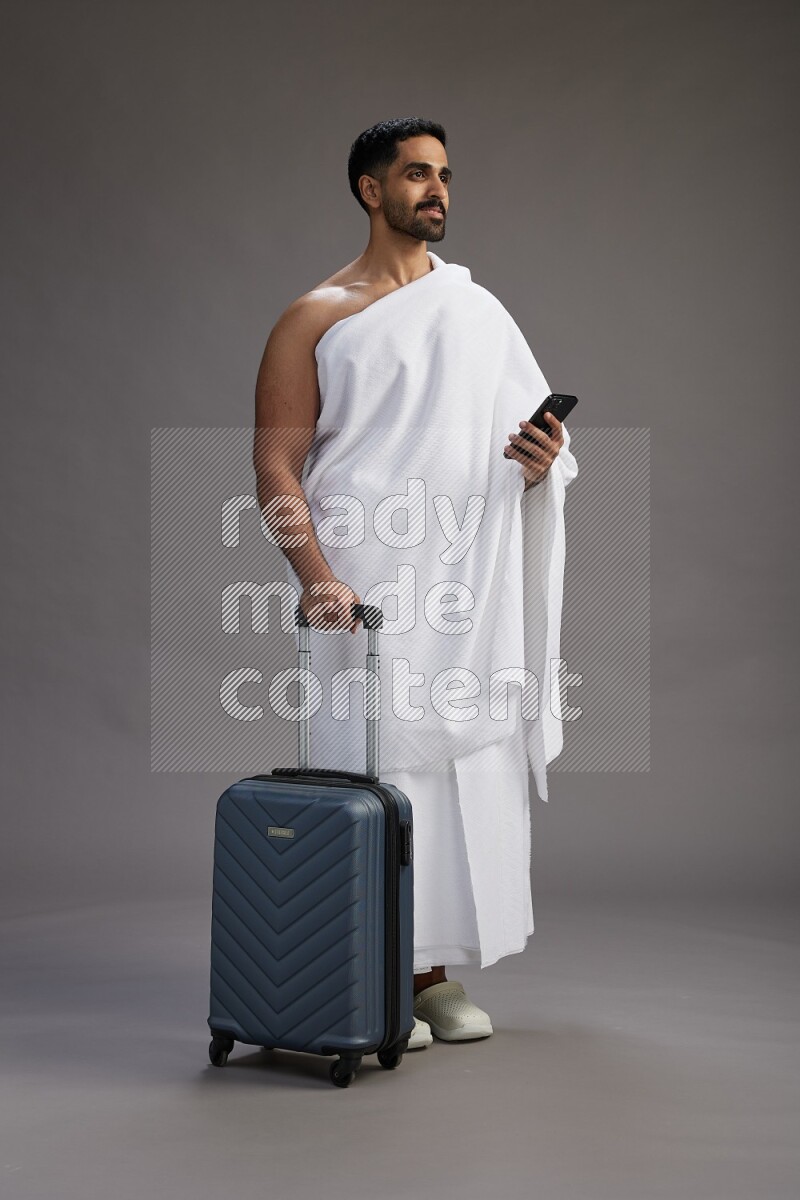 A man wearing Ehram Standing holding traveling bag on gray background