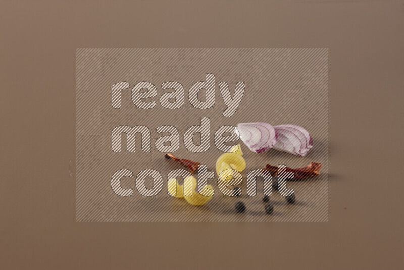 Raw pasta with different ingredients such as cherry tomatoes, garlic, onions, red chilis, black pepper, white pepper, bay laurel leaves, rosemary and cardamom on beige background