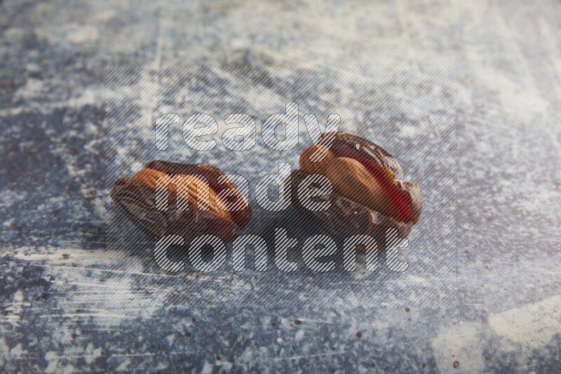 two almond stuffed madjoul dates on a rustic blue background
