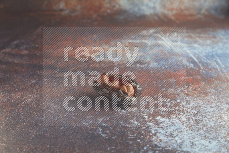 one hazelnut stuffed madjoul date on a rustic reddish background