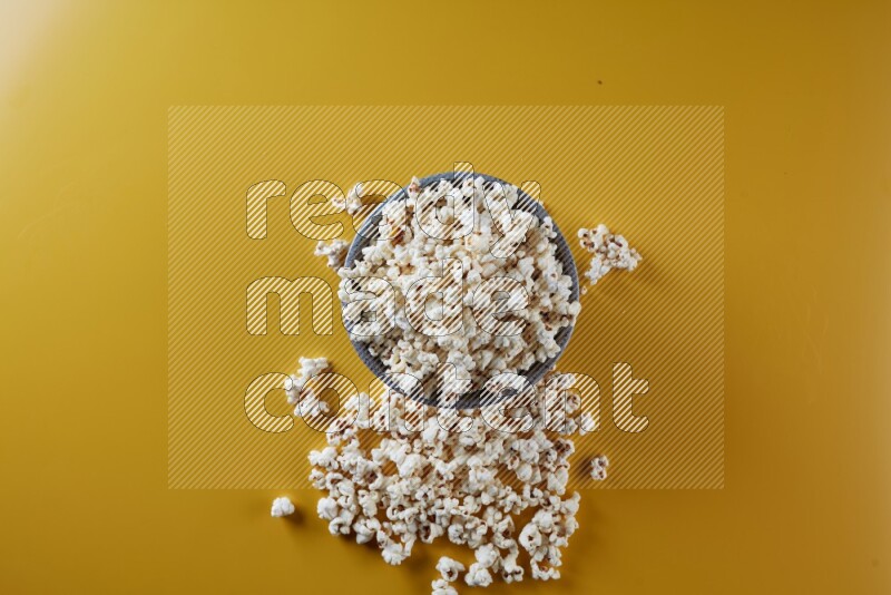 A multicolored pottery bowl full of popcorn with popcorn beside it on a yellow background in different angles