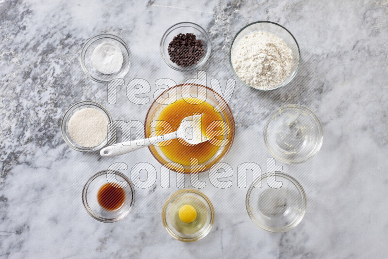 كوكيز خطوة بخطوة بمكوناتها، الدقيق، الزبدة، السكر البني، البيض، الفانيليا، السكر الأبيض، رقائق الشوكولاتة وصودا الخبز على خلفية رخام رمادي