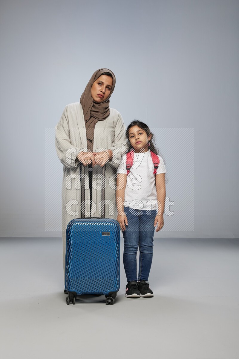 Mom and daughter standing pulling a carry-on bag on gray background