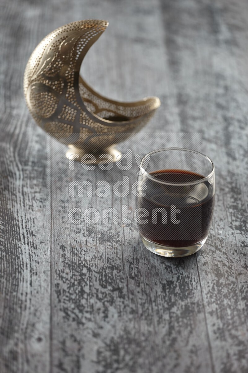 A silver lantern with different drinks, dates, nuts, prayer beads and quran on grey wooden background