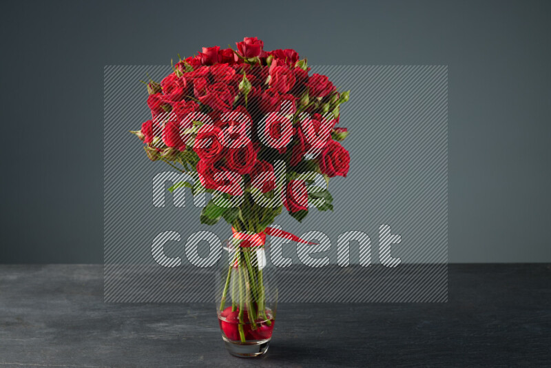 An arrangement of vivid red roses tightly bound with a red ribbon in a glass vase on black marble background