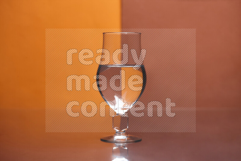 The image features a clear glassware filled with water, set against orange and dark orange background