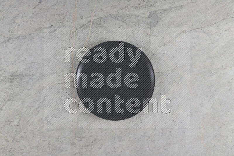 A black ceramic circular plate on grey marble background