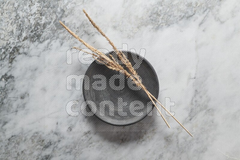 Wheat stalks on black pottery plate on grey marble background