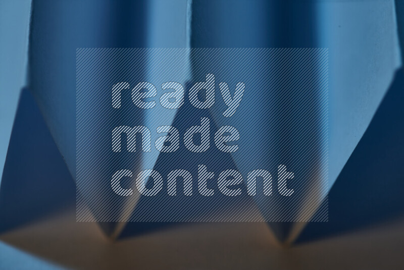 صورة مجردة مقربة تظهر طيات ورقية هندسية حادة بتدرجات اللون الأزرق مع درجات لونية دافئة