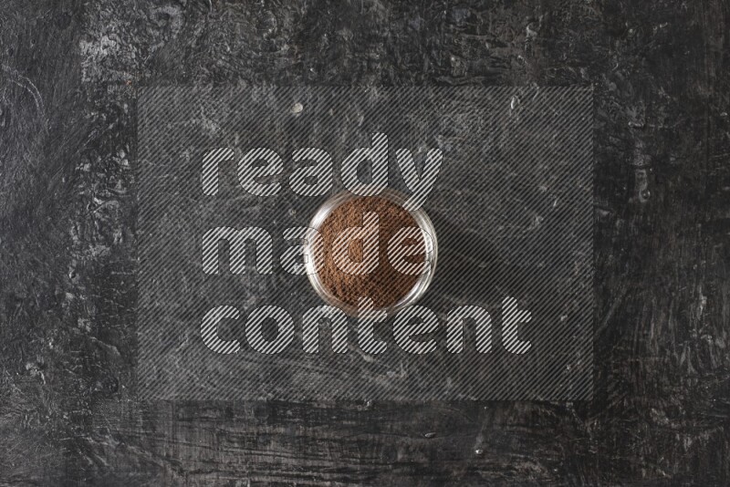A glass jar full of cloves powder on a textured black flooring