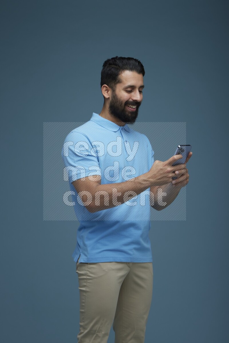 A man Texting on his phone in a blue background wearing a Blue shirt