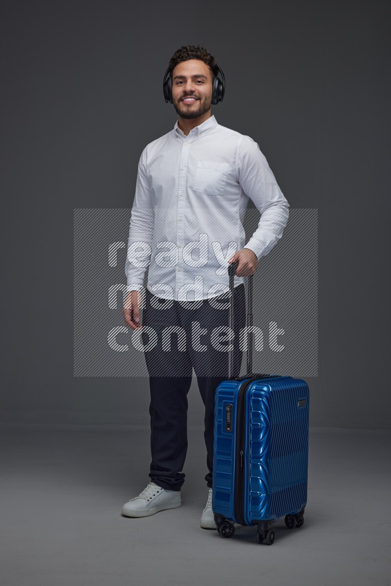 A man Posing with a carry-on with headsets  Wearing a White shirt on a grey background