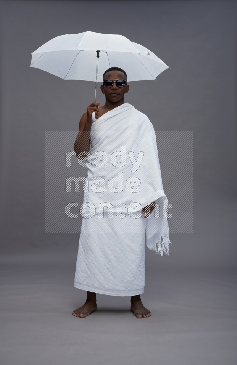 A man wearing Ehram Standing holding umbrella on gray background