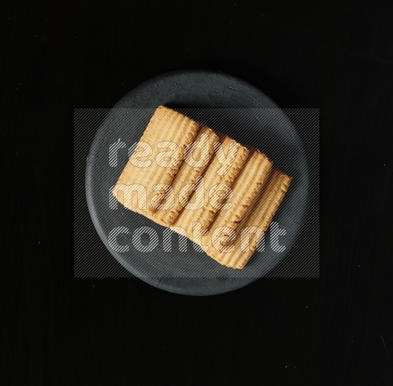 Golden biscuits in a black pottery plate on black background