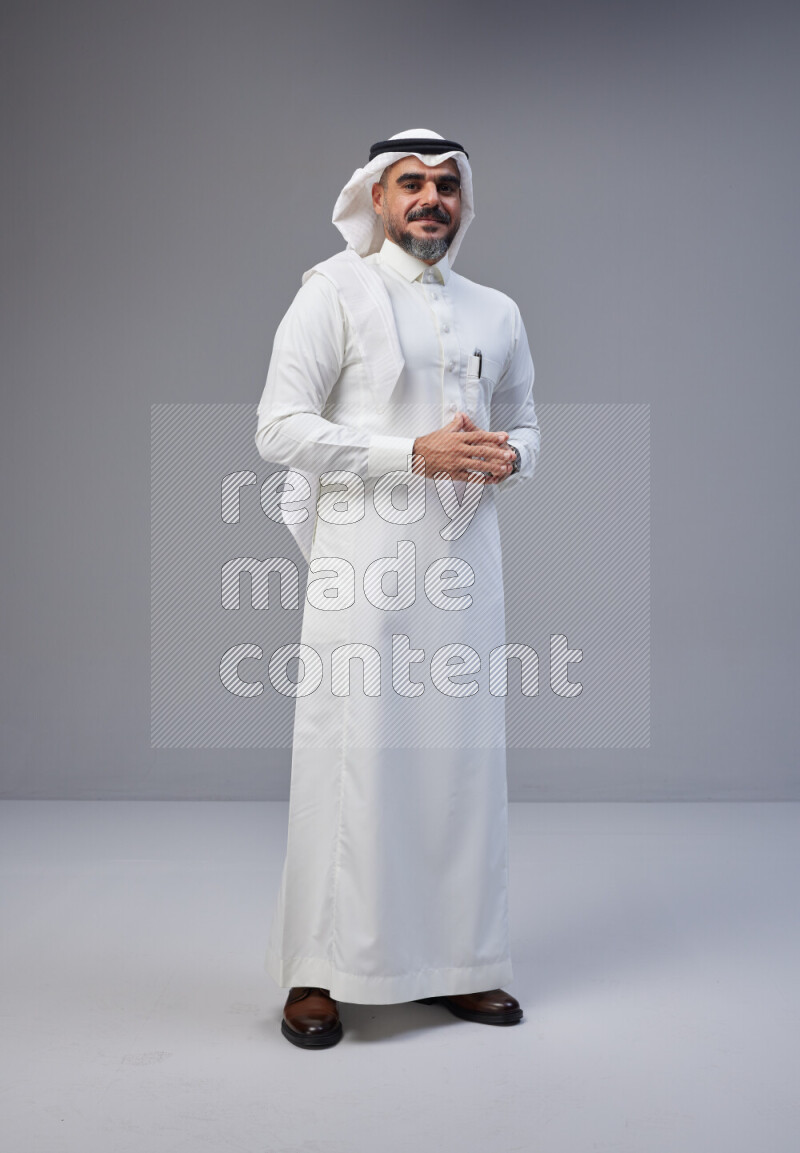 Saudi man Wearing Thob and white Shomag standing interacting with the camera on Gray background
