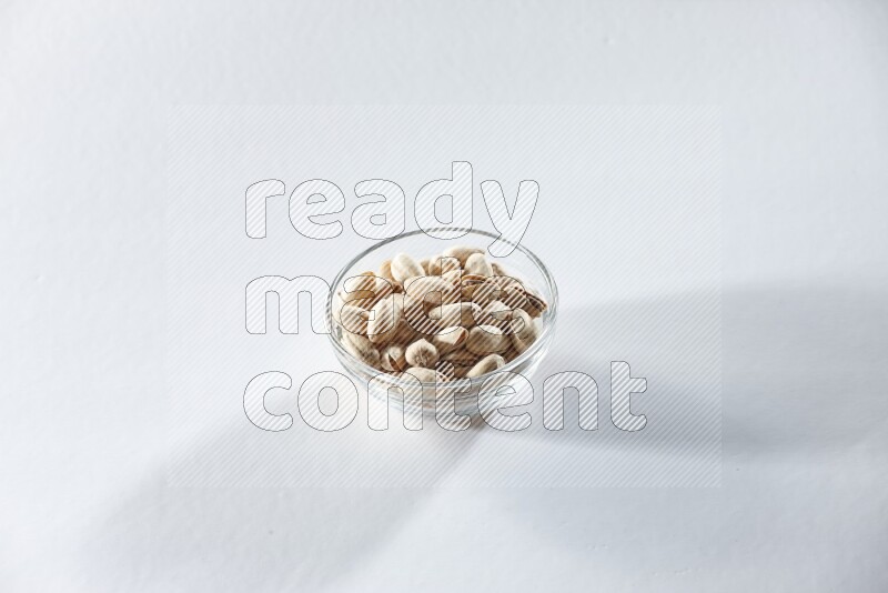 A glass bowl full of pistachios on a white background in different angles