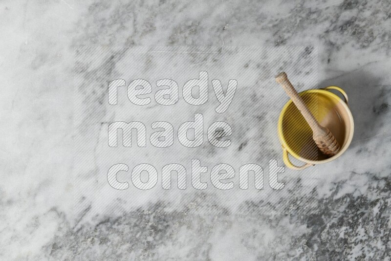 Multicolored pottery bowl with wooden honey dipper in it on grey marble background