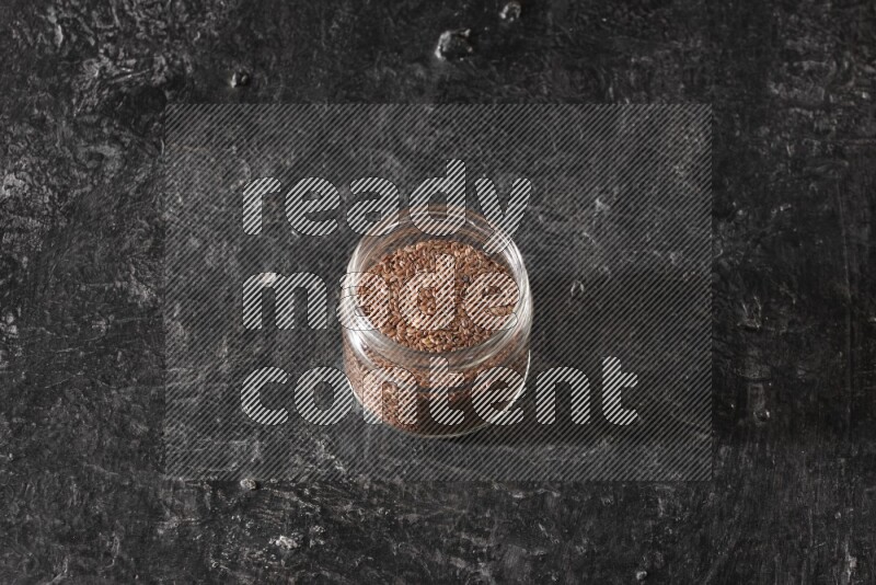 A glass jar full of flaxseeds on a textured black flooring