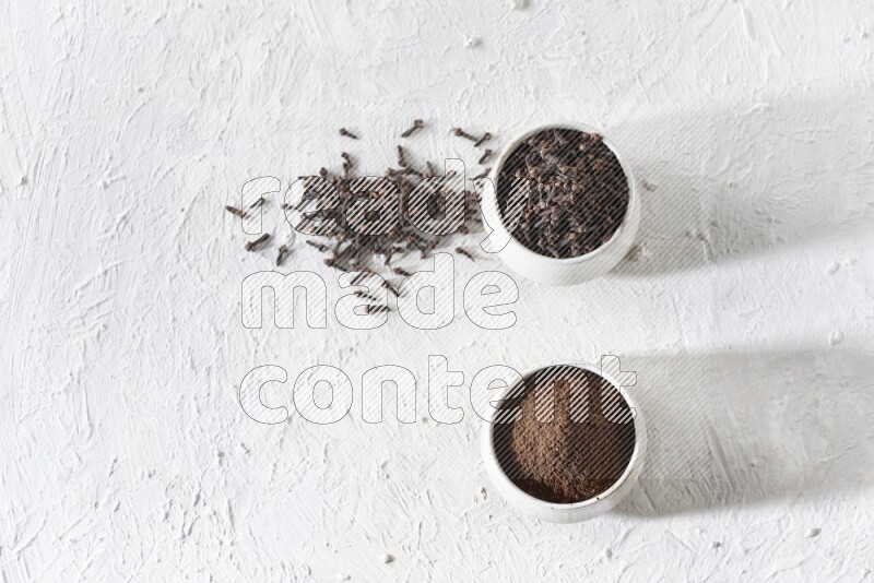 2 Beige ceramic bowls, one full of cloves and the other full of powder on textured white flooring