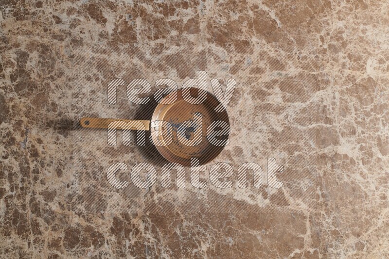 A small copper pan on beige marble background