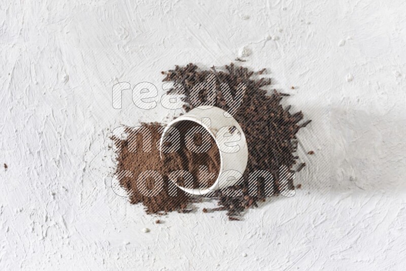 A beige ceramic bowl with cloves powder spilled out of it on a textured white flooring
