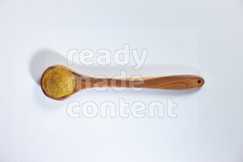 A wooden ladle full of turmeric powder on white flooring