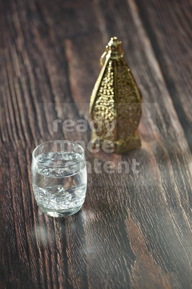 A golden lantern with different drinks, dates, nuts, prayer beads and quran on brown wooden background