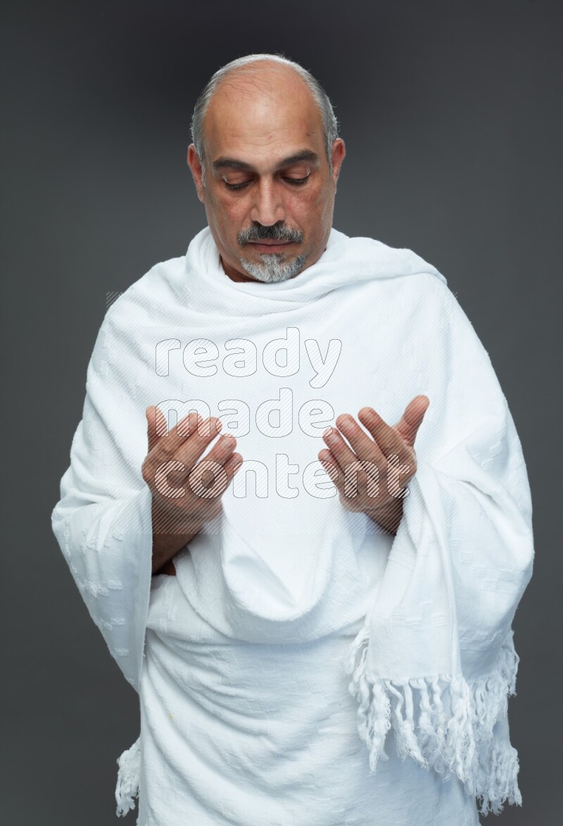 A man wearing Ehram Standing dua'a on gray background