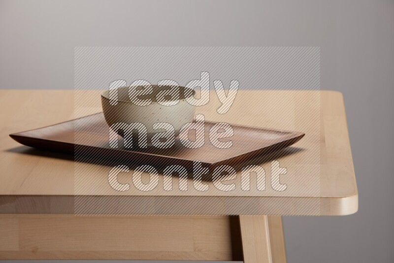 multicolored bowl placed on a rectangular wooden tray on the edge of wooden table
