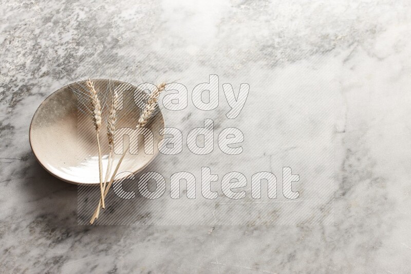 Wheat stalks on multicolored pottery plate on grey marble background
