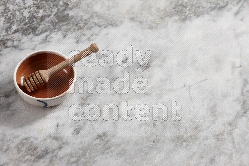 وعاء فخاري متعدد الألوان مع ملعقة عسل خشبية بداخله على خلفية من الرخام الرمادي