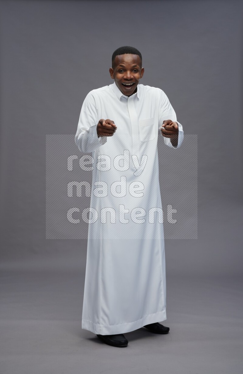 Saudi man wearing thob standing interacting with the camera on gray background