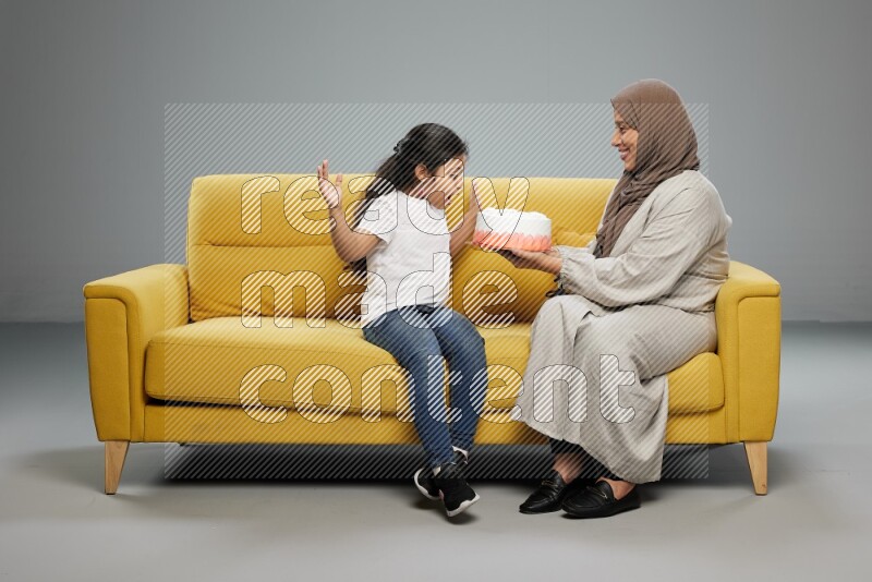 A girl sitting giving a cake to her mother on gray background