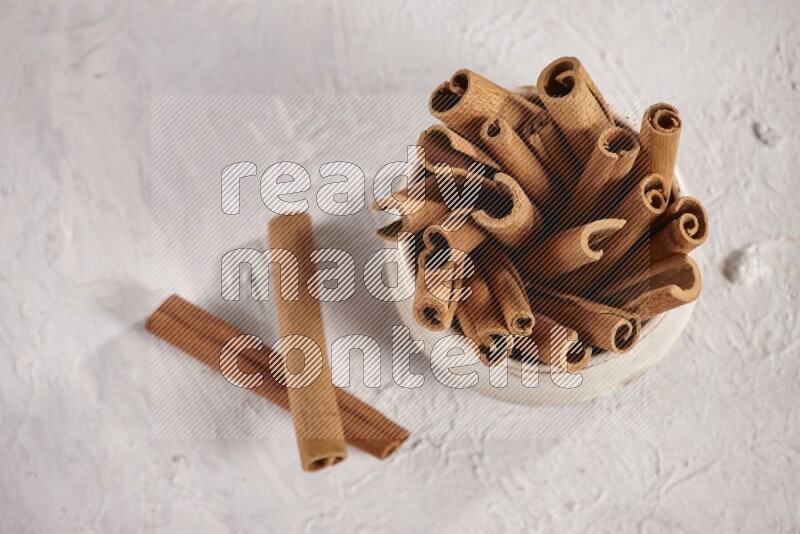Cinnamon sticks in a beige bowl and more sticks beside it on white background