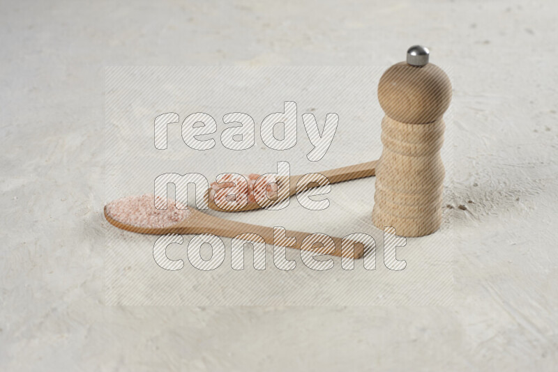 2 wooden spoons filled with fine and coarse salt with wooden grinder beside them on white background