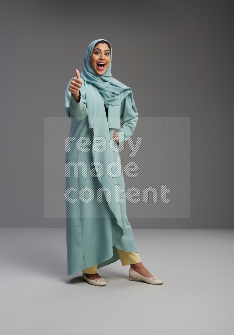 Saudi Woman wearing Abaya standing interacting with the camera on Gray background