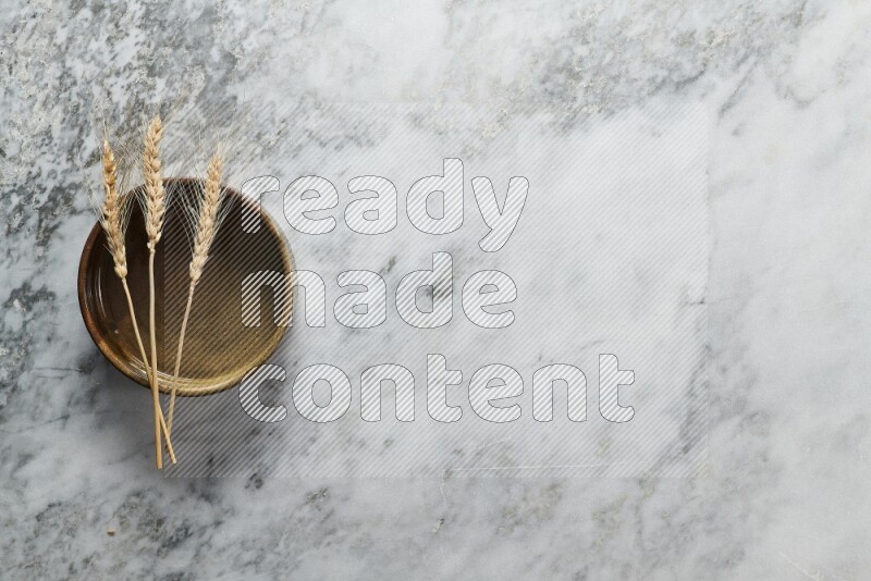 Wheat stalks on multicolored pottery oven plate on grey marble background