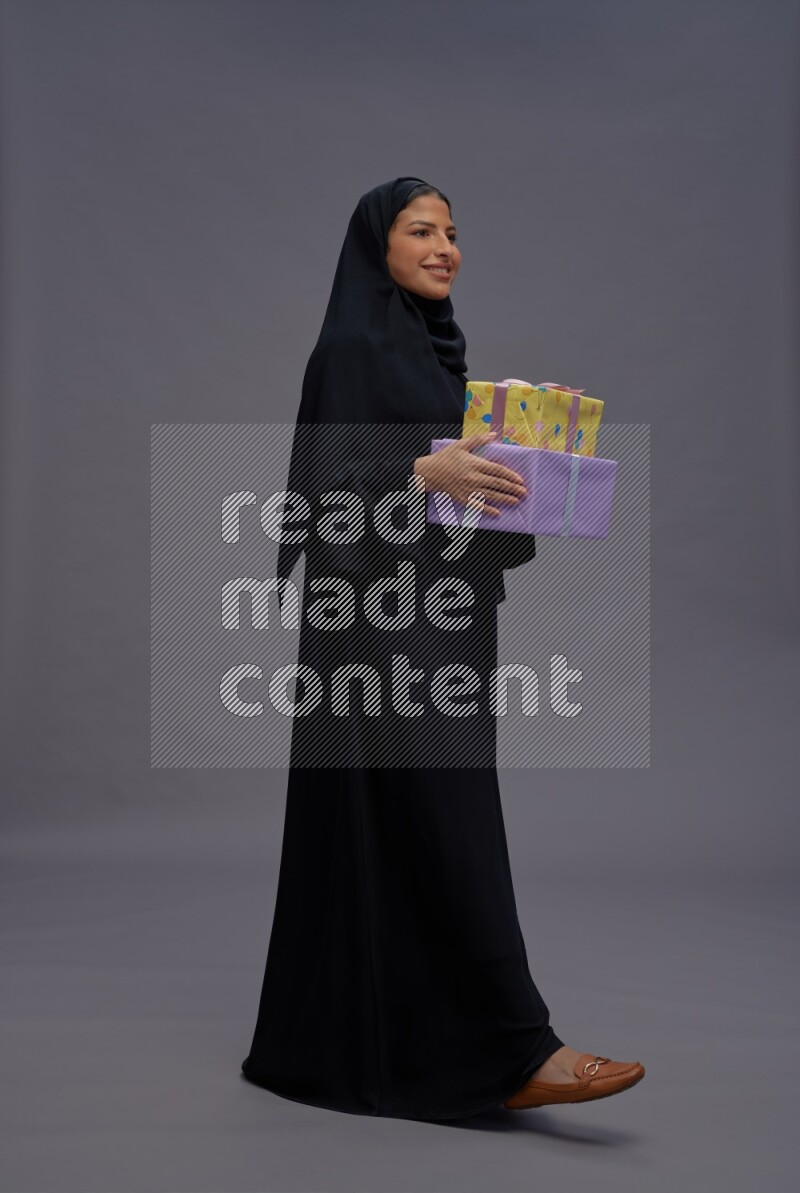 Saudi woman wearing Abaya standing holding gift box on gray background