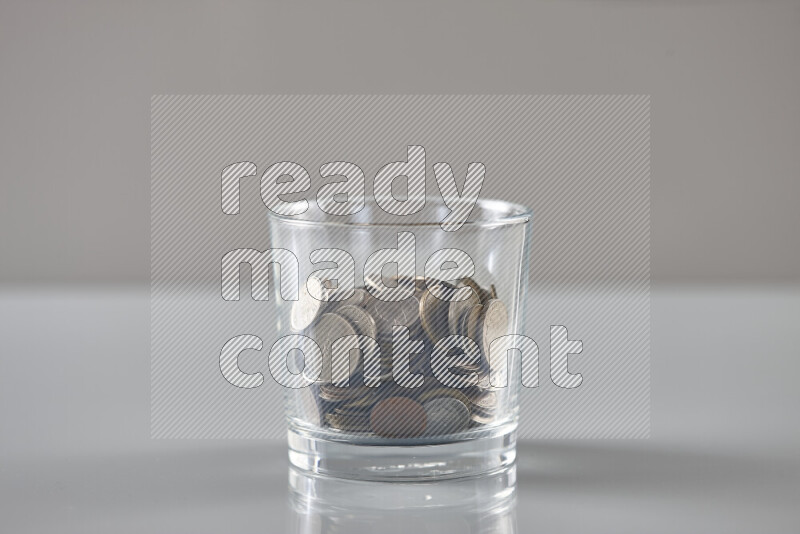 Random old coins in a glass cup on grey background