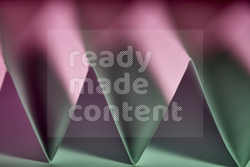 A close-up abstract image showing sharp geometric paper folds in green and purple gradients