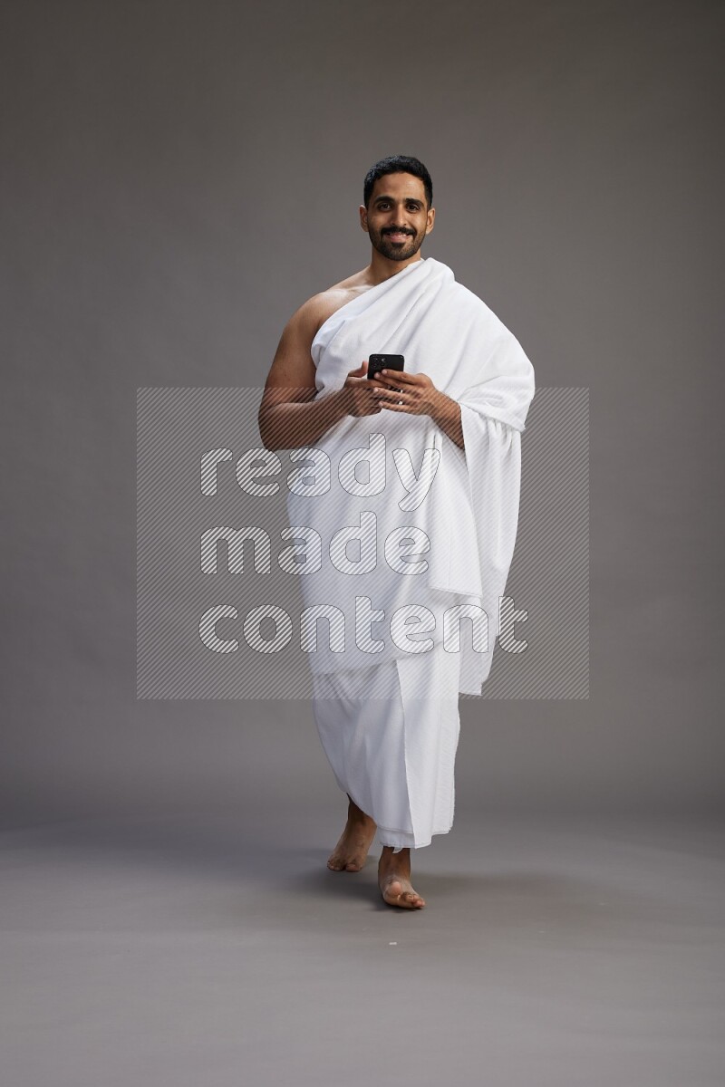 A man wearing Ehram Standing texting on phone on gray background