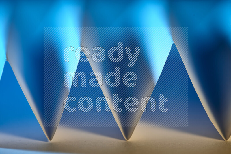 A close-up abstract image showing sharp geometric paper folds in blue gradients and warm tones