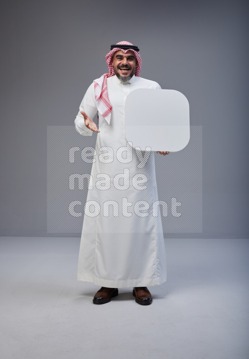 Saudi man Wearing Thob and red Shomag standing holding social media sign on Gray background