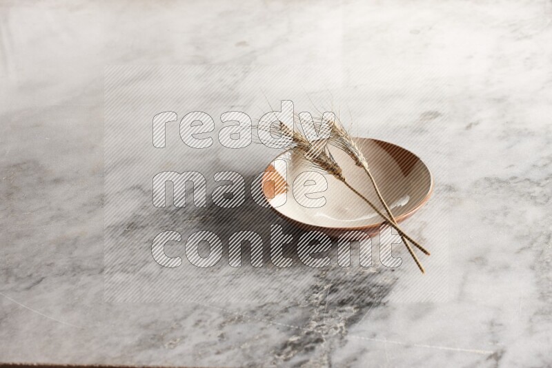 Wheat stalks on multicolored pottery plate on grey marble background