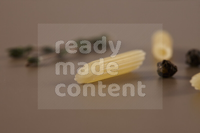 Raw pasta with different ingredients such as cherry tomatoes, garlic, onions, red chilis, black pepper, white pepper, bay laurel leaves, rosemary and cardamom on beige background