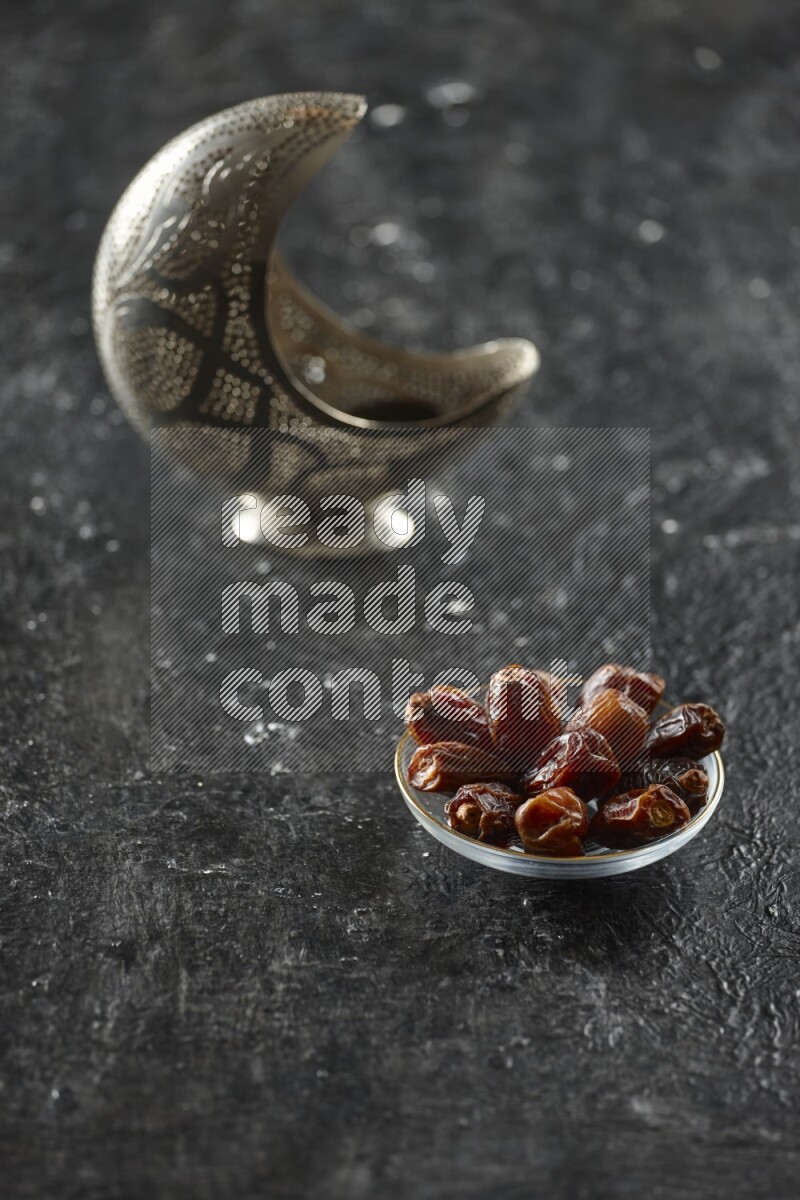 A silver lantern with different drinks, dates, nuts, prayer beads and quran on textured black background